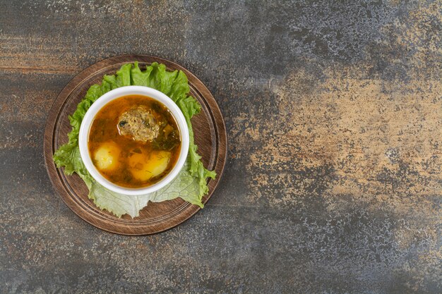 Bol de soupe aux boulettes de viande sur planche de bois.