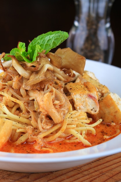 Bol de soupe blanc avec des spaghettis et des morceaux de pain décorés de légumes verts