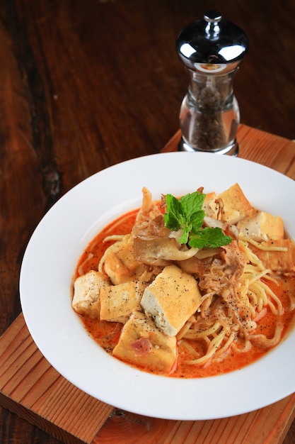 Bol de soupe avec des morceaux de pain, de la viande et des spaghettis décorés de légumes verts