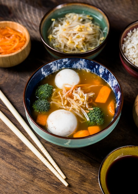 Photo gratuite bol de soupe de poisson et de poisson, servi avec pousses de haricots et carotte râpée sur une table en bois