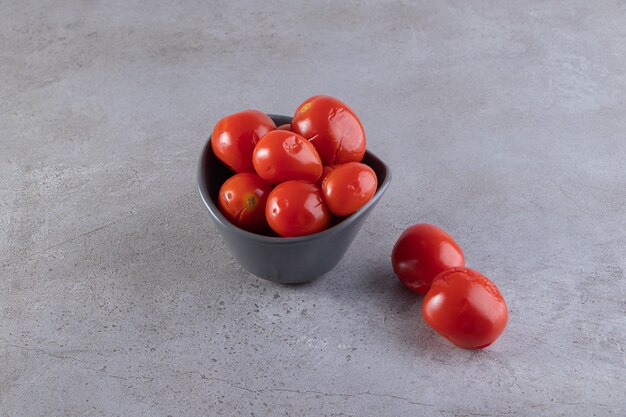 Bol de tomates marinées placé sur une surface en pierre.