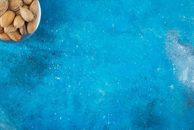Un bol en verre d'amandes décortiquées, sur la table bleue.