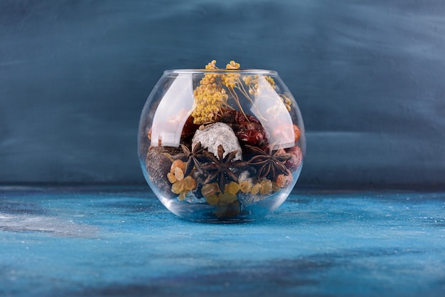 Bol en verre avec fleurs séchées et fruits sur table bleue.