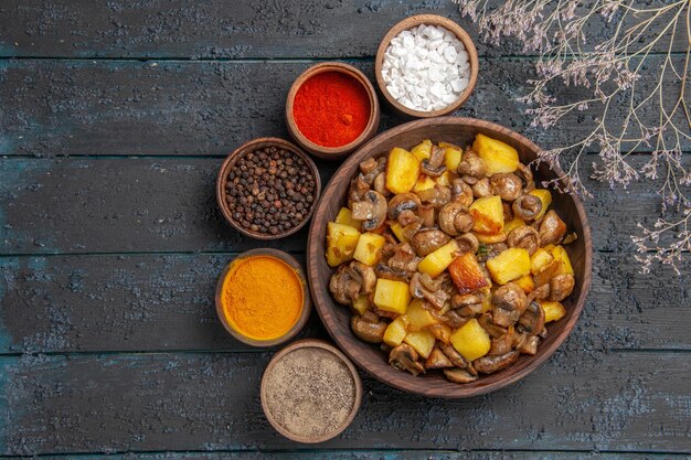 Bol avec vue de dessus avec bol de nourriture et d'épices avec pommes de terre et champignons et épices colorées autour à côté des branches d'arbres