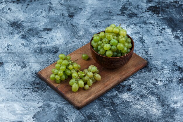 Bol de vue grand angle de raisins blancs sur une planche à découper sur fond de marbre bleu foncé. horizontal