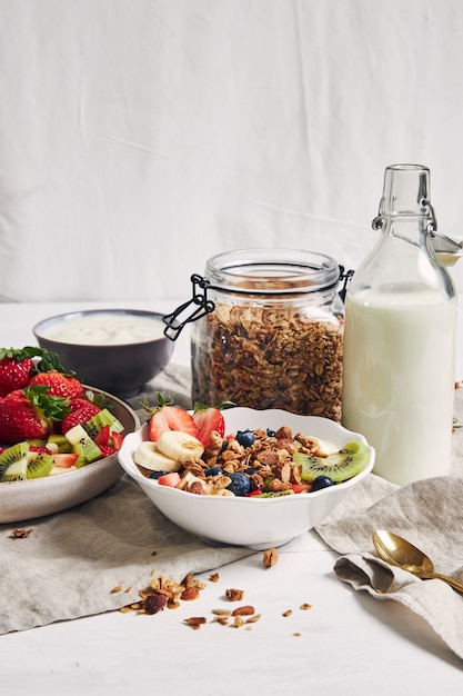 Photo gratuite bols de granola avec du yogourt, des fruits et des baies sur une surface blanche