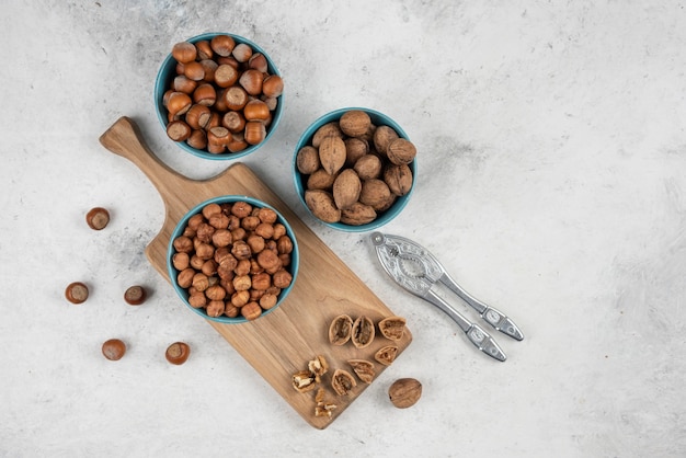 Photo gratuite bols de noix, de noisettes et de noyaux sur une planche à découper en bois.