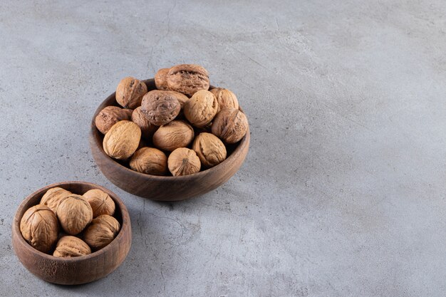 Bols pleins de noix saines en coque placés sur une table en pierre.