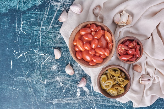 Bols de tomates marinées et jalapenos sur bleu avec de l'ail et de la nappe. Vue de dessus.