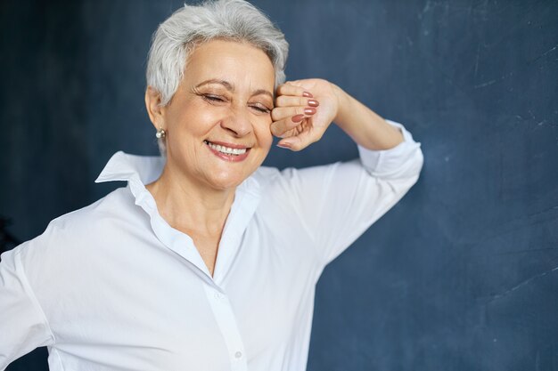 Bon à la recherche de femme d'âge moyen réussie en chemise blanche posant, touchant le visage et souriant