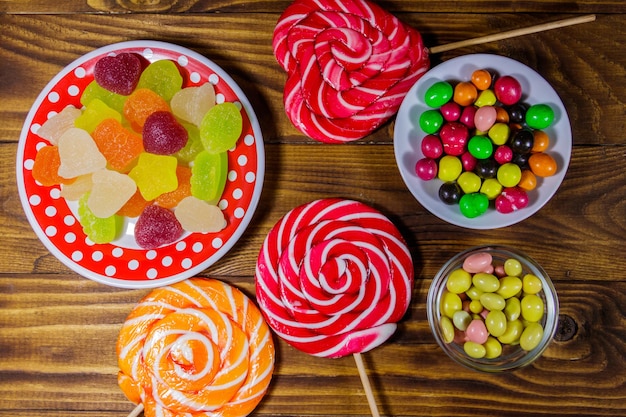 Bonbons au chocolat colorés, sucettes et bonbons à la gelée sur table en bois