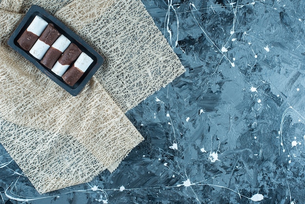 Bonbons bicolores sur une plaque en bois sur une nappe , sur la table bleue.