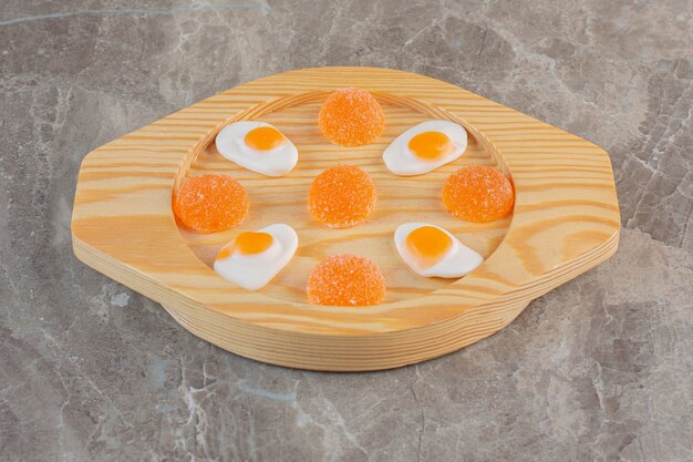 Bonbons blancs et oranges sur une plaque en bois sur une surface grise.