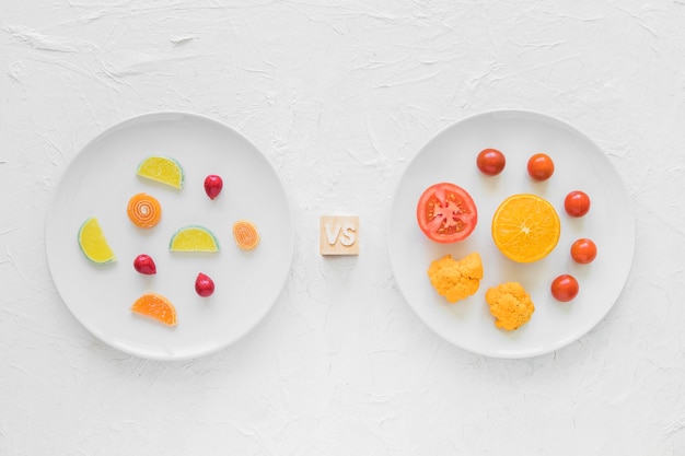 Bonbons colorés contre des légumes frais sur une plaque blanche sur fond