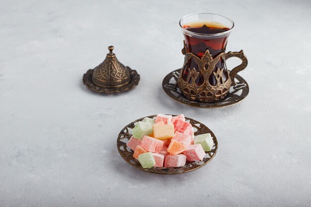 Bonbons à la gelée servis avec un verre de thé sur une surface blanche.