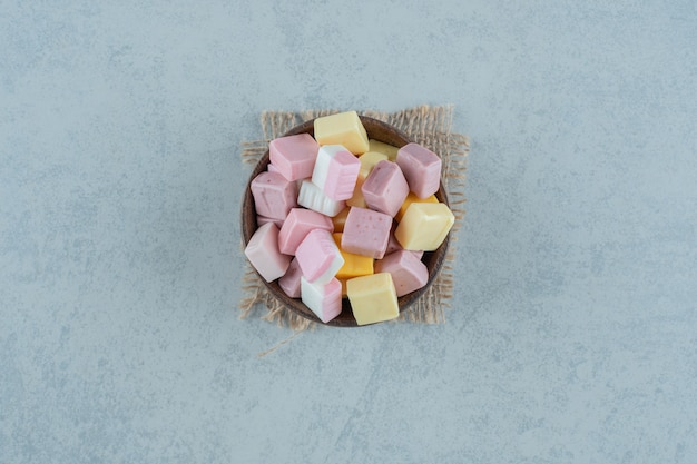 Bonbons à la guimauve rose et jaune dans un bol en bois sur une surface blanche