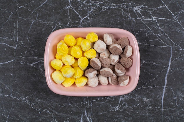 Bonbons jaunes et bruns dans le bol, sur la surface en marbre
