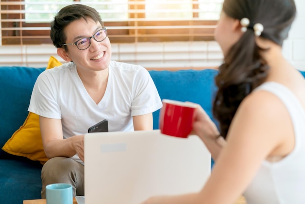 Bonheur couple asiatique famille se marier profiter de la conversation du matin avec amour et relation sur le canapé avec ordinateur portable et café fond intérieur de la maison