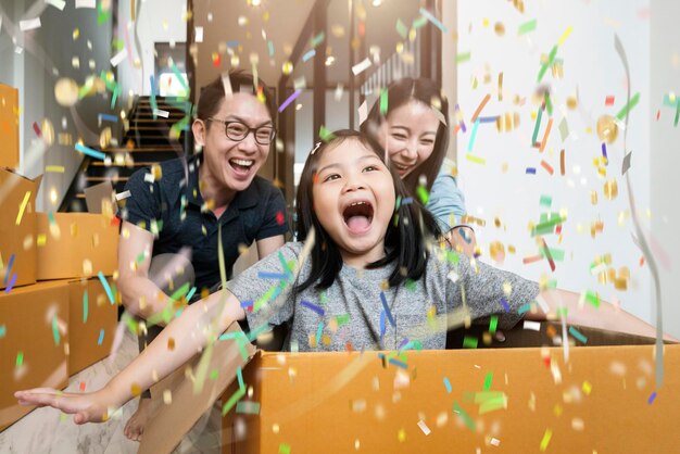 Bonheur famille asiatique maman papa fille emménageant dans une nouvelle maison main transporter une boîte de trucs avec une expression joyeuse et amusante