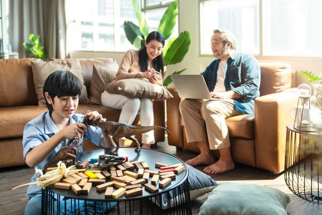 Bonheur fils enfant jouant pendant que les parents se détendent ensemble sur le canapé à la maison souriant garçon actif divertissant avec des dinosaures jouets sur le sol famille heureuse passant du temps ensemble dans le salon le week-end