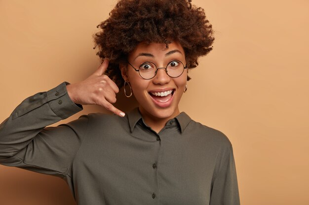 Bonjour, je vous entends. Une femme ravie et heureuse imite l'appel téléphonique, fait un geste mobile près de l'oreille, sourit joyeusement, aime la communication à distance, vêtue d'une chemise sombre, des lunettes transparentes.