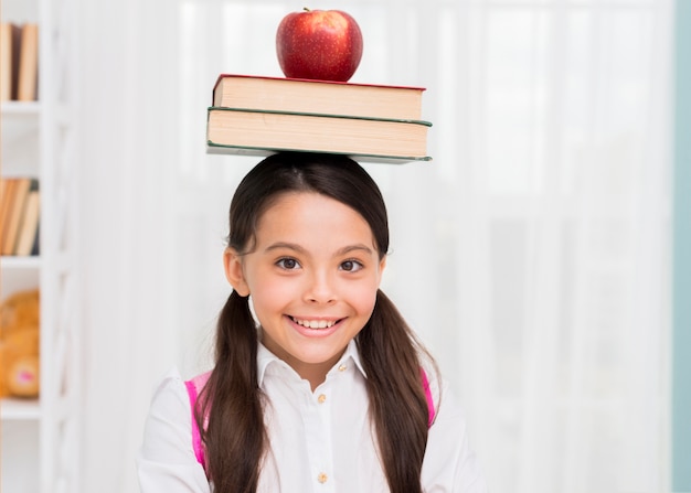 Bonne écolière avec des livres et pomme sur la tête