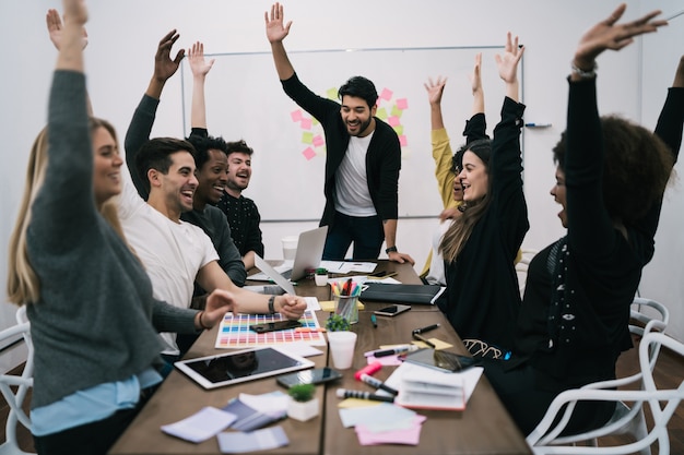 Bonne équipe commerciale célébrant avec les mains levées au bureau. Succès et concept gagnant.