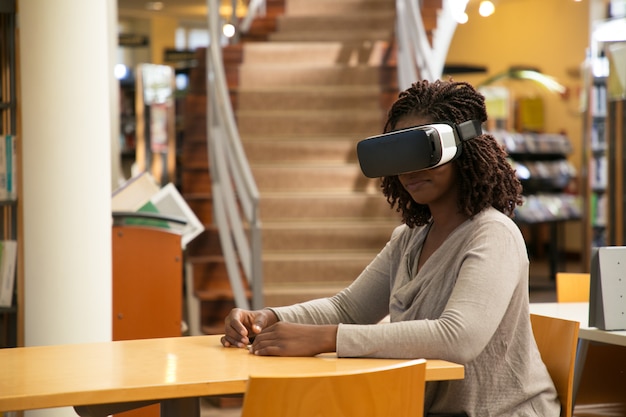 Bonne étudiante bénéficiant d'une expérience de réalité virtuelle dans une bibliothèque