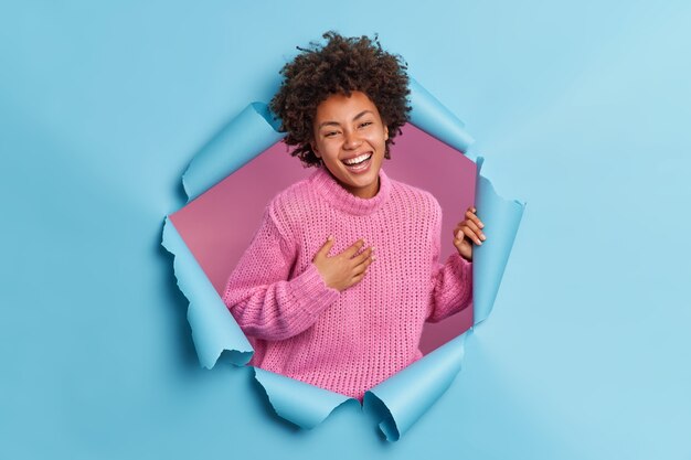 Bonne femme positive avec des cheveux afro sourit largement garde la main sur la poitrine