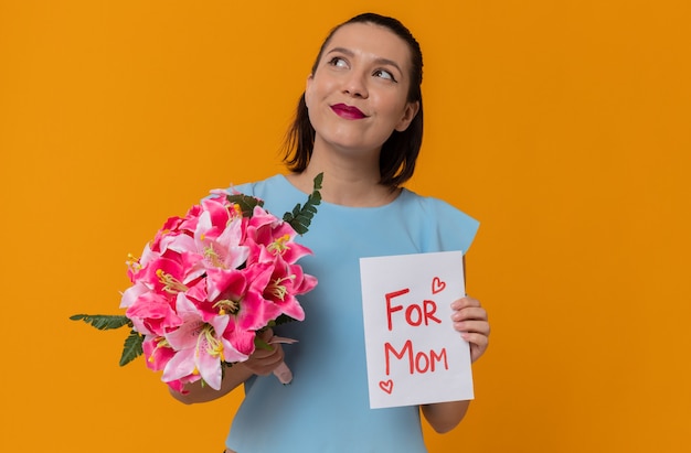 Bonne fête des mères. heureuse jolie jeune mère tenant un bouquet de fleurs et une carte de voeux avec texte : pour maman