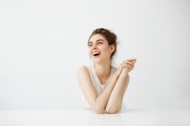 Bonne humeur jeune belle femme avec chignon souriant rire assis à table sur fond blanc.