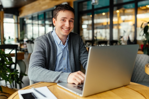 Bonne humeur pour bien travailler. Beau jeune homme travaillant sur son ordinateur portable