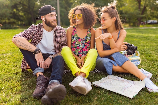 Bonne jeune entreprise d'amis assis dans le parc, l'homme et la femme s'amusant ensemble, style de mode hipster d'été coloré, voyageant avec appareil photo, parlant, souriant