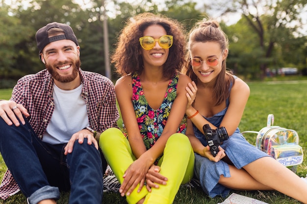 Photo gratuite bonne jeune entreprise d'amis assis dans le parc, l'homme et la femme s'amusant ensemble, voyageant avec appareil photo, parlant, souriant