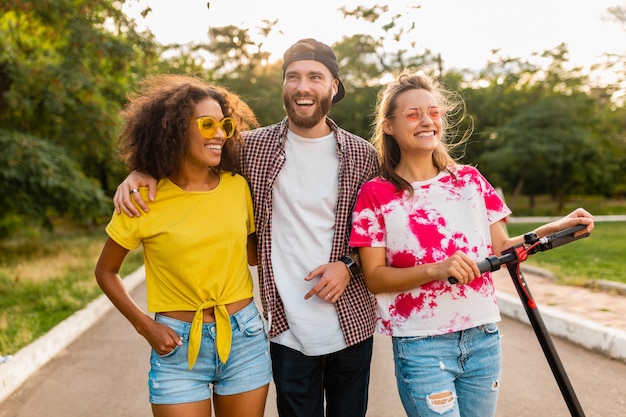 Photo gratuite bonne jeune entreprise d'amis souriants marchant dans le parc avec scooter électrique, homme et femme s'amusant ensemble