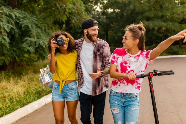 Bonne jeune entreprise d'amis souriants marchant dans le parc avec scooter électrique, homme et femme s'amusant ensemble