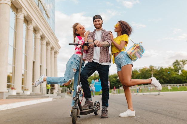 Bonne jeune entreprise d'amis souriants marchant dans la rue avec scooter électrique, homme et femme s'amusant ensemble