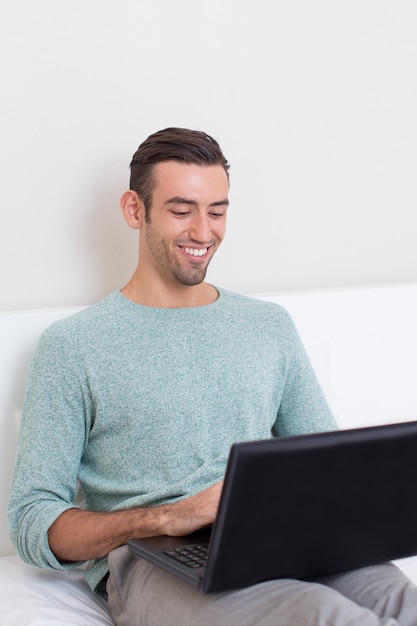 Bonne jeune homme travaillant sur ordinateur portable sur canapé