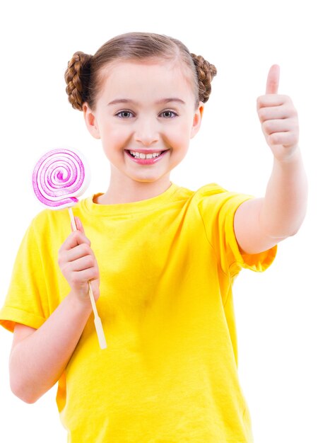 Bonne jolie fille en t-shirt jaune avec des bonbons colorés montrant les pouces vers le haut signe - isolé sur blanc