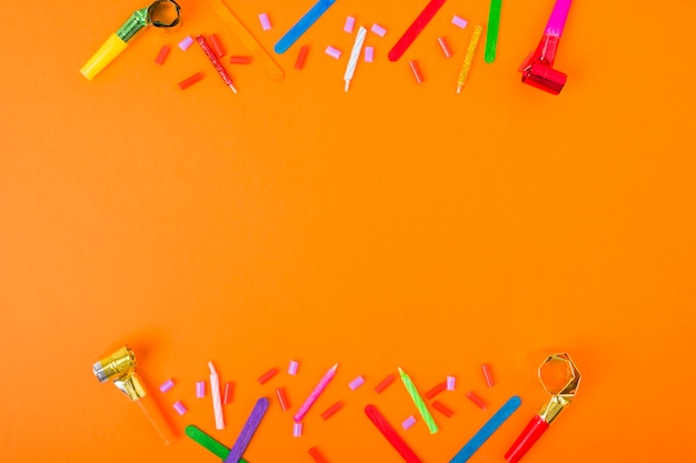 Bordure faite avec des bougies, des bonbons, soufflant corne et bâton de crème glacée sur un fond orange