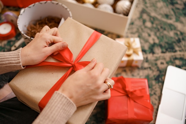 Bouchent les mains féminines attachant un arc de ruban rouge sur une boîte-cadeau artisanale.