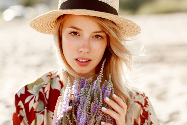 Bouchent le portrait de beauté de la belle fille blonde romantique appréciant l'odeur parfaite de lavande. Concept de soins de la peau et cosmétique. Couleurs chaudes du coucher du soleil.