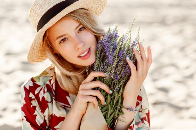 Bouchent le portrait de beauté de la belle fille blonde romantique appréciant l'odeur parfaite de lavande. Concept de soins de la peau et cosmétique. Couleurs chaudes du coucher du soleil.