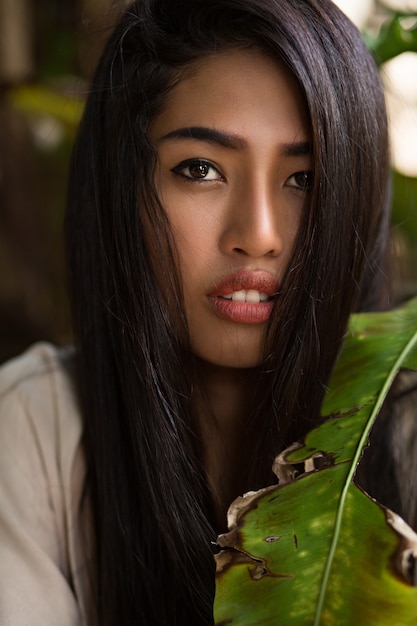 Bouchent le portrait de beauté d'une femme asiatique avec une peau parfaite posant dans un jardin tropical. Des cheveux sains, des lèvres charnues.