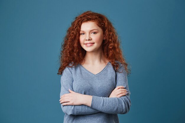 Bouchent le portrait de la belle étudiante aux cheveux roux et taches de rousseur en chemise grise croisant les mains, regardant avec une expression heureuse et joyeuse.