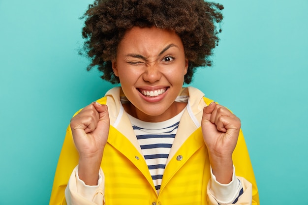 Photo gratuite bouchent le portrait d'une belle femme énergique cligne des yeux, soulève les sourcils, serre les poings avec succès, se sent très heureux