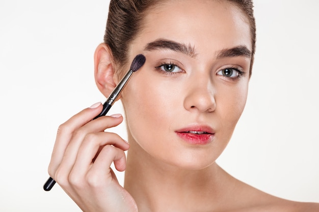 Bouchent portrait de belle femme avec une peau saine appliquant maquillage yeux de peinture avec pinceau