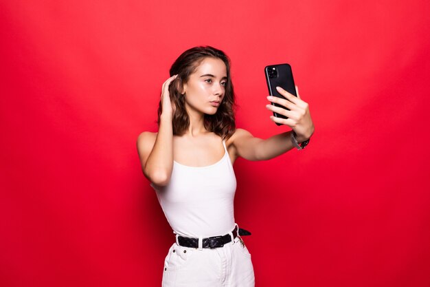 Bouchent portrait belle femme prendre selfie devant smartphone moderne isolé sur mur rouge brillant