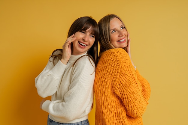 Bouchent Le Portrait De Deux Jolies Femmes En Pulls Confortables Posant Sur Jaune. Tendances Mode Automne Et Hiver.