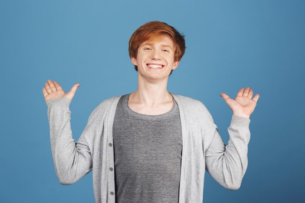 Bouchent le portrait du jeune étudiant aux cheveux roux heureux et joyeux en tenue décontractée élégante, écartant les mains avec une expression excitée, voyant le meilleur ami après une longue période.